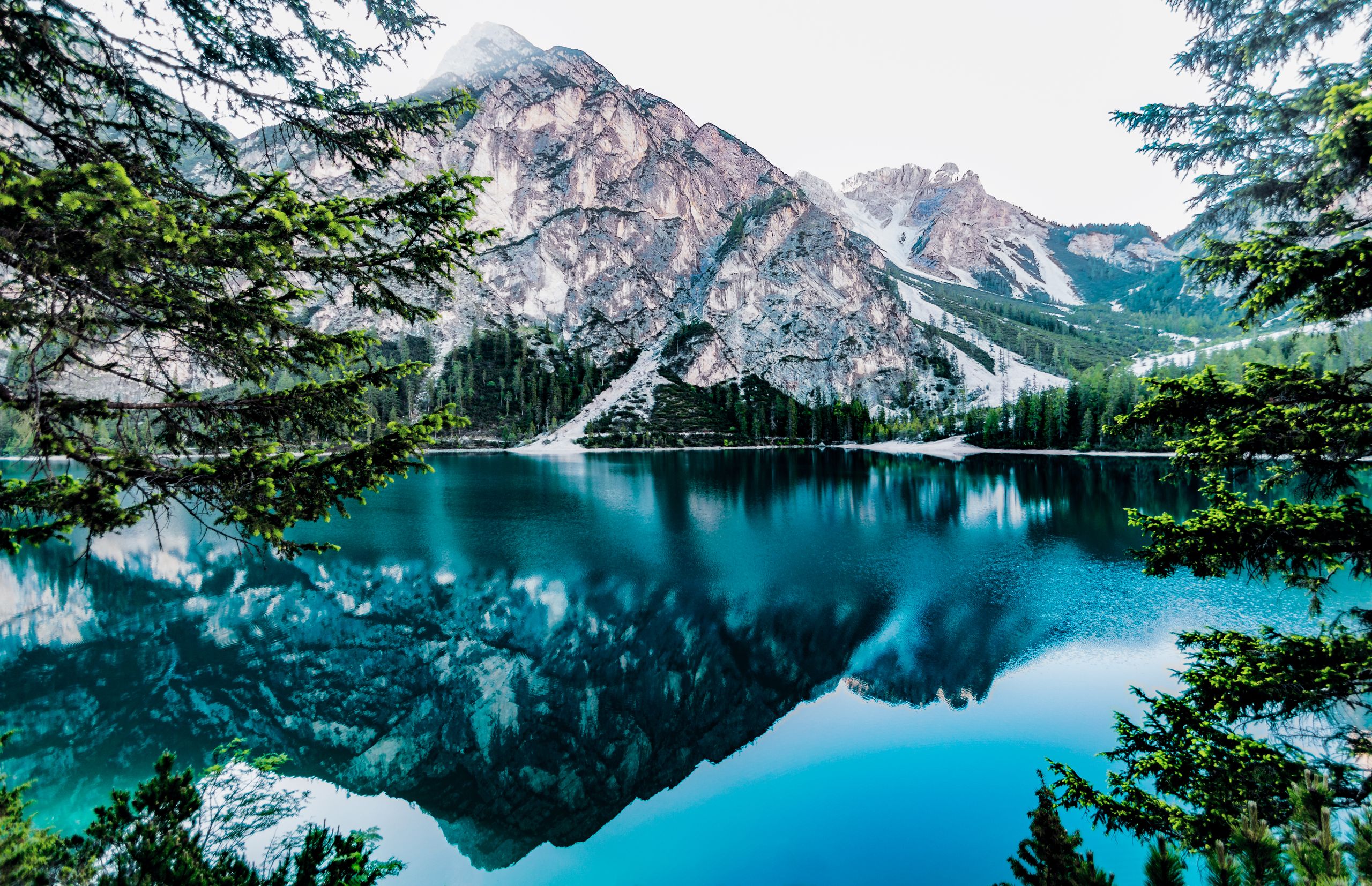 Agua turquesa del lago de Braies y reflejos de las cumbres entre los árboles
